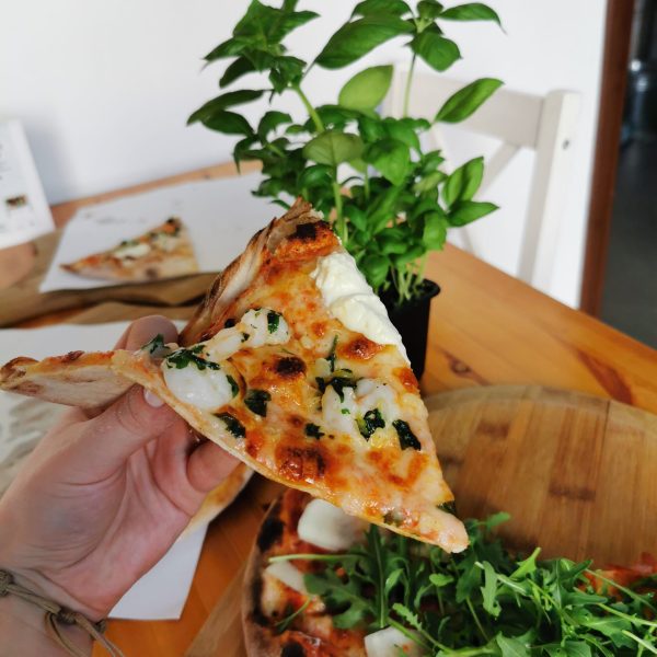 kawałek pizzy z włoskimi składnikami w tym rukolą oraz buratta