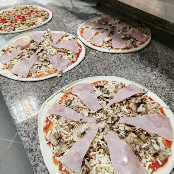 pizza w trakcie przygotowania z włoską szynką i pieczarkami